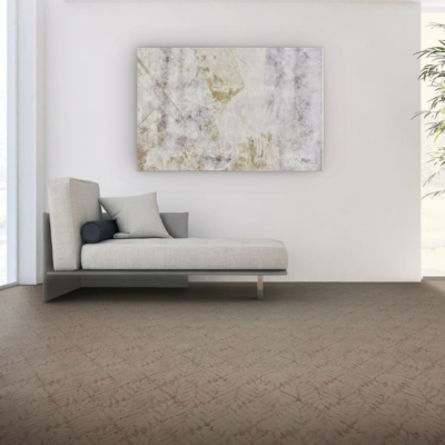 A minimalist lounge area featuring a light beige carpet with subtle patterns, a contemporary chaise lounge with beige cushions, abstract wall art, and natural light from large windows.
